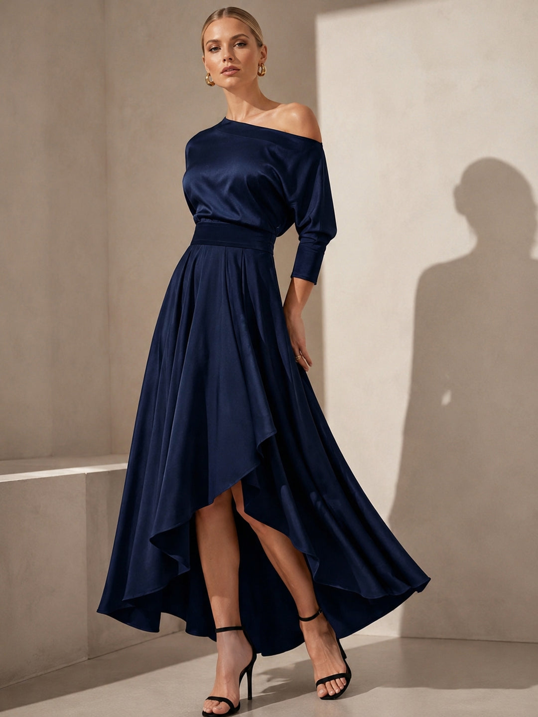 A woman wearing a navy, one-shoulder, 3/4 sleeve, asymmetrical hemline satin dress suitable for mother of the bride or groom.